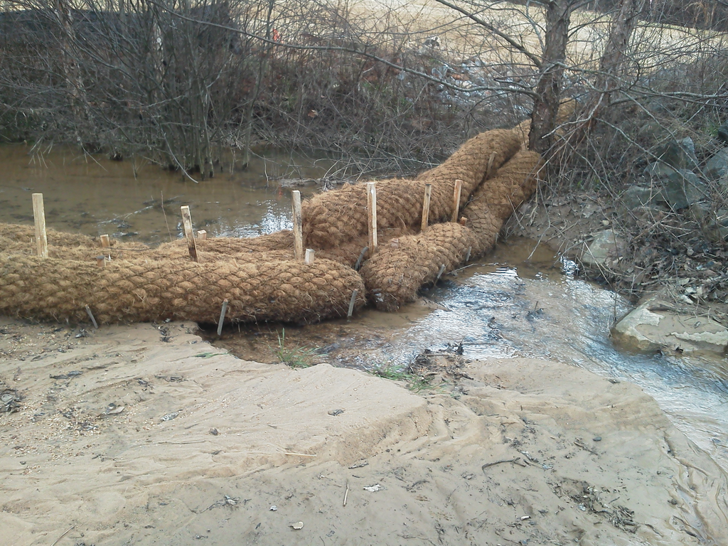 Erosion control products, including coir logs and jute mesh matting, slow erosion in the existing stream. Silt that used to end up in Lake Norman is visible in the foreground of the photo.