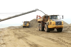 The machines are running tirelessly, loading earth and sand that arrives at the island by barge before being transferred to the fleet of Volvo haulers for delivery to the required deposit points. The trucks travel along an uneven haul road approximately 0.6 miles long, and then unload at the jobsite.