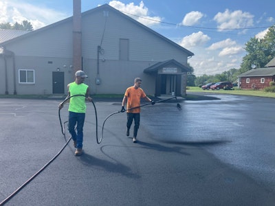 Pave Care employees Claude Whiteside and Christian Shaffer seal coating at Beloved Disciple Catholic Church.