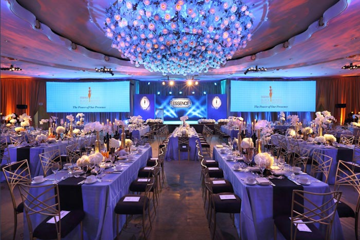 For Essence's sixth annual pre-Oscar award luncheon, Candace Purdie Montgomery worked with Caravents to drape the Beverly Hills Hotel in a rich palette of gold, black, and slate blue, reflected in the ballroom, lounge, custom linens, screen graphics, and lighting effects. A recurring motif of ornate gold frames decked the space, from the press wall to sponsor integrations in the lounge to the stage set. For the first time, the table configuration included a mix of round and rectangular tables, making the room feel larger.