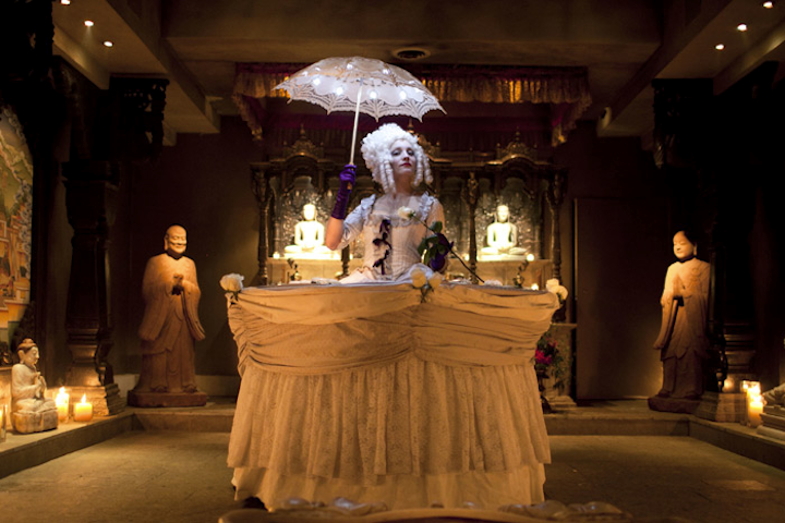 Chicago’s Redmoon Theater—renown for its dreamlike events—showcases “Table Ladies” as part of its Redmoon for Hire program, from which planners can source the theater’s collection of performers, atmospheric elements, and “food service performance devices” for private and corporate events. The Table Ladies are two corseted and wigged performers who circulate among guests wearing Victorian-inspired, oversize hoop skirts that act as tables to display appetizers or desserts. Similar food displays are also available through Redmoon, such as “Floating Trays” (hardwood surfaces attached to backpacks) and “Briefcase Servers” (open briefcases featuring miniature puppet shows within the lids). Pricing ranges from $1,200 to $3,600 for the Table Ladies, from $1,200 for the Floating Trays, and from $700 to $1,800 for the Briefcase Servers; services are available in the Chicago area.