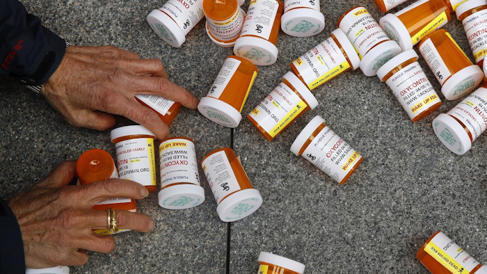 In this Friday, April 5, 2019, file photo, a protester gathers containers that look like OxyContin bottles at an anti-opioid demonstration in front of the U.S. Department of Health and Human Services headquarters in Washington, D.C. Image credit: AP Photo/Patrick Semansky