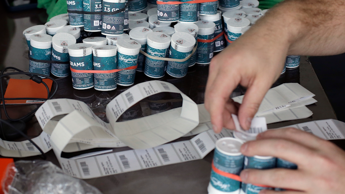 Mike Whittaker, of Quincy, Mass., director of operations at Pure Oasis recreational marijuana shop, applies bar codes to containers of cannabis flowers in the store, Sunday, March 8, 2020, in Boston. Pure Oasis, Boston's first recreational marijuana shop, and the state's first black-owned one, is slated to open, Monday, March 9, 2020.