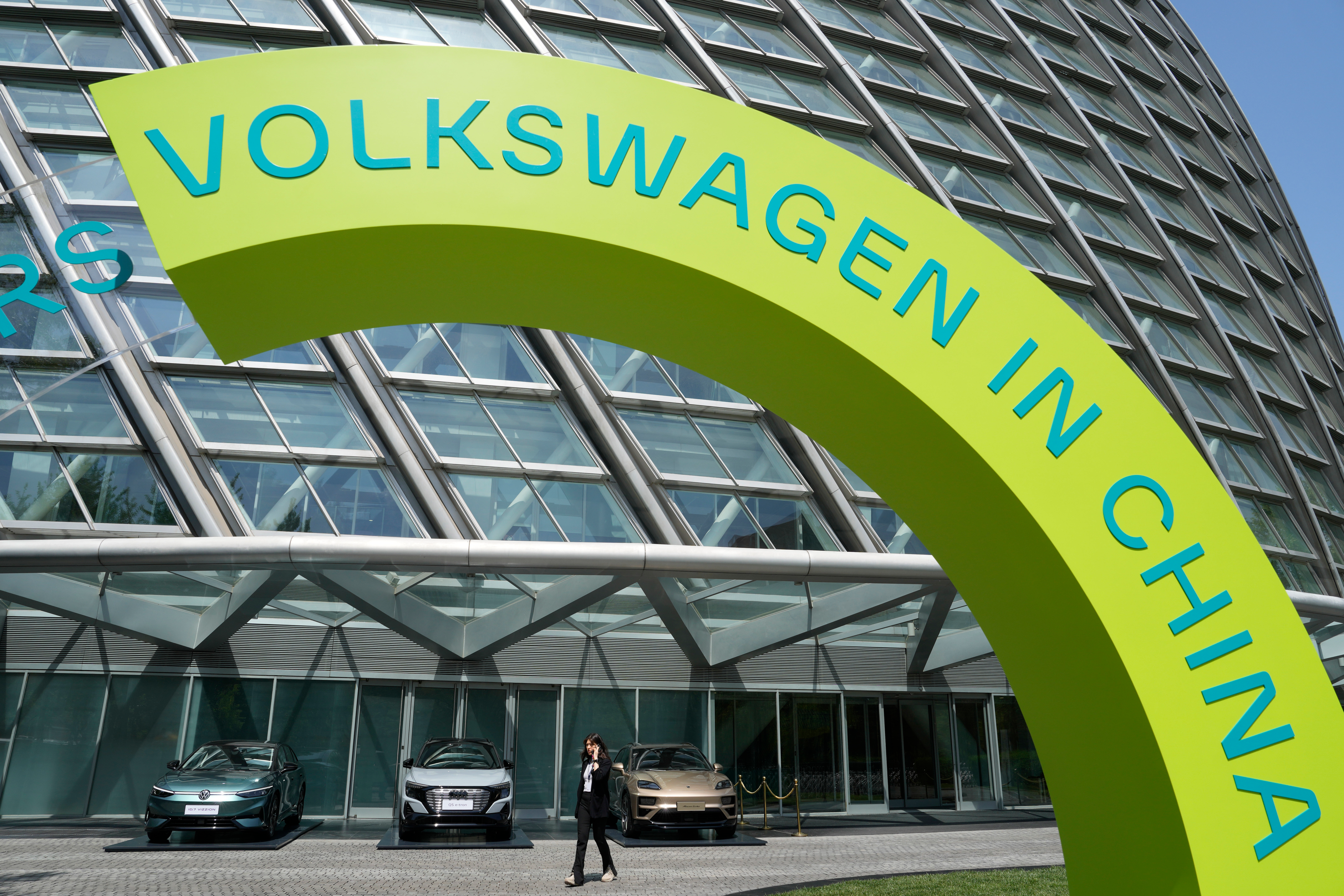 A woman walks past cars on display at a Volkswagen event ahead of the auto show in Beijing, Wednesday, April 24, 2024.