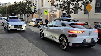 Two Waymo driverless taxis stop before passing one another on a San Francisco street on Feb. 15, 2023.