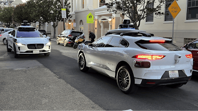 Two Waymo driverless taxis stop before passing one another on a San Francisco street on Feb. 15, 2023.