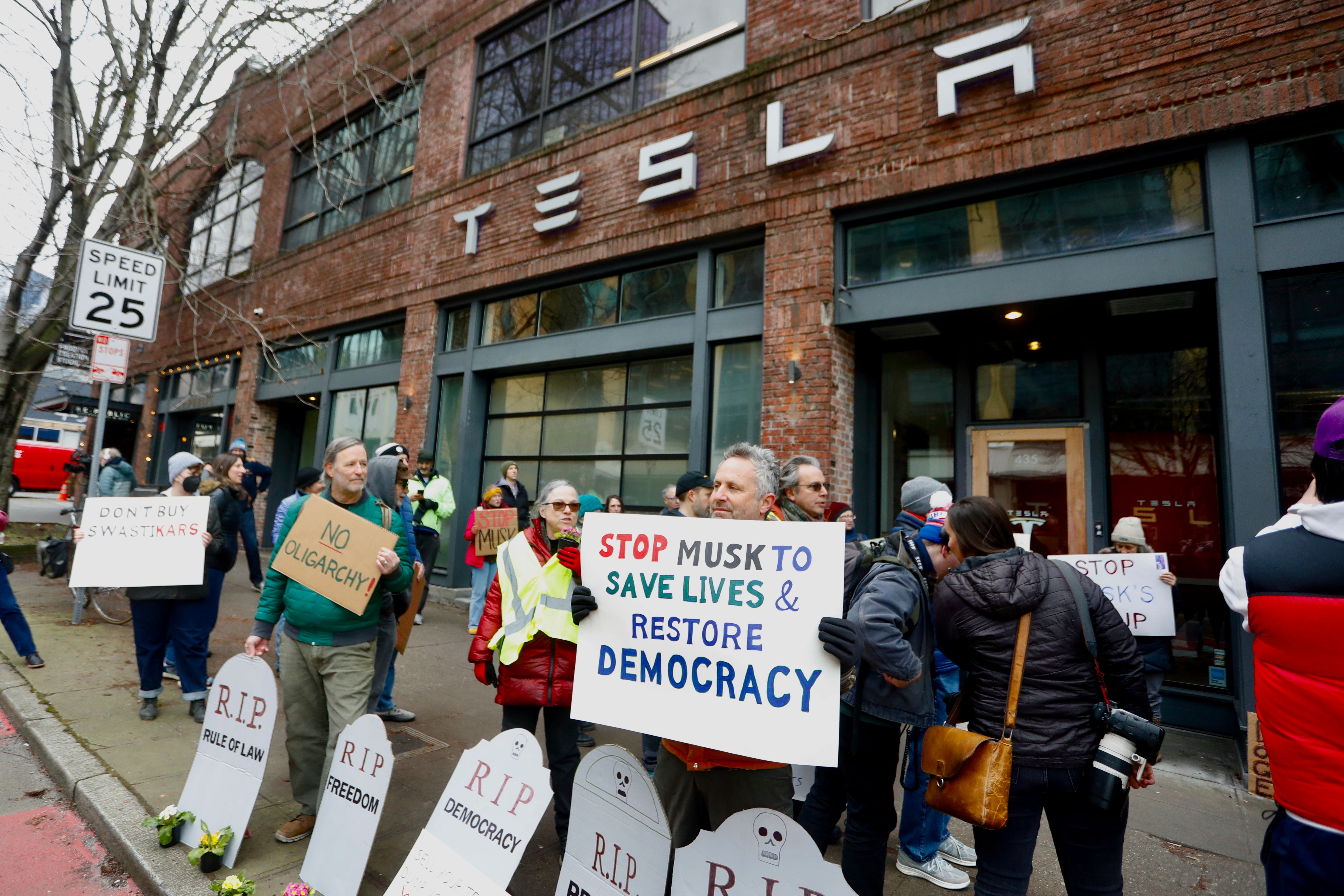 People protesting Elon Musk's actions in the Trump administration hold signs outside a Tesla showroom in Seattle on Thursday, Feb. 13, 2025.