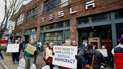 People protesting Elon Musk's actions in the Trump administration hold signs outside a Tesla showroom in Seattle on Thursday, Feb. 13, 2025.
