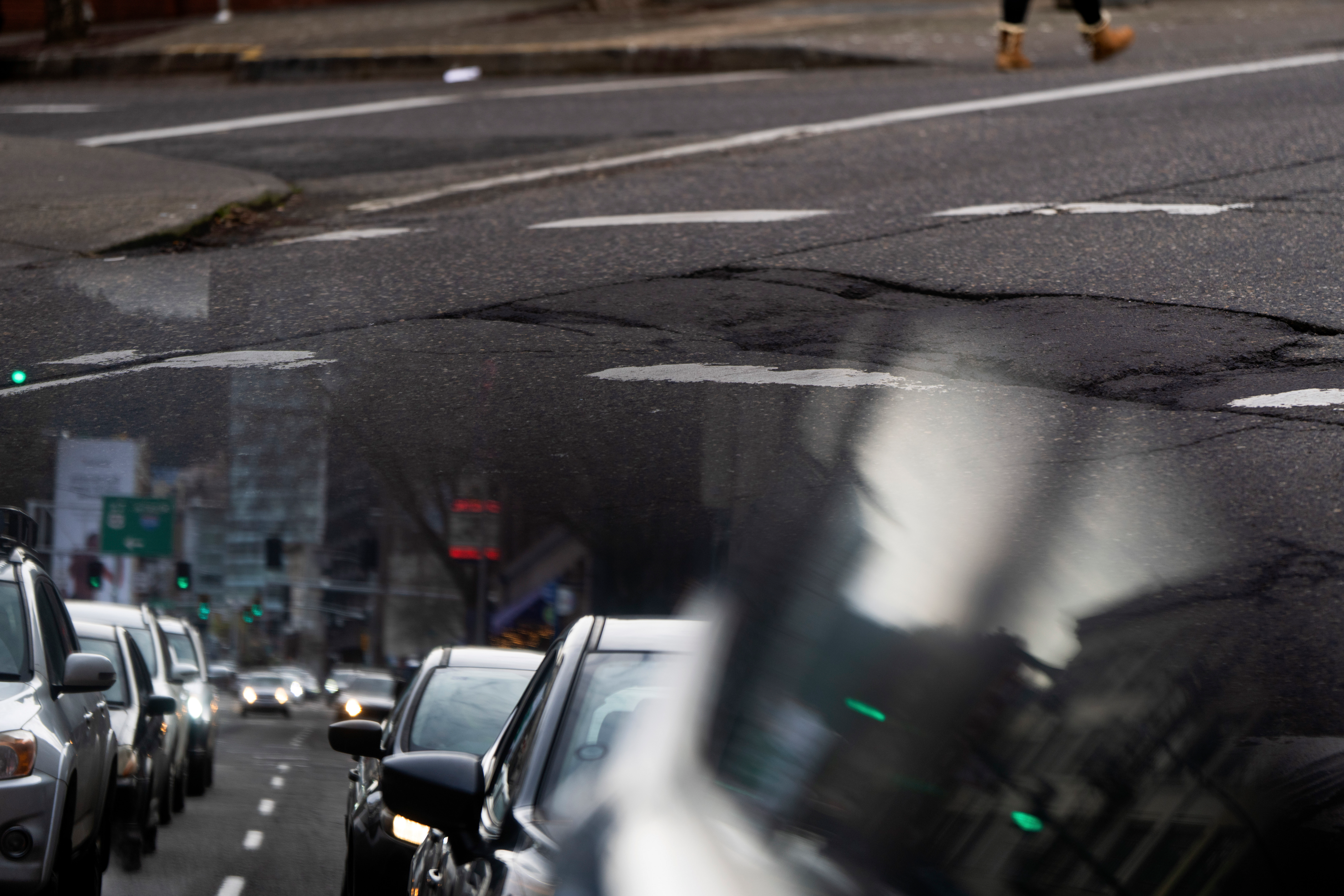 In this image taken through the reflection of a car window, a person walks along W Burnside Street near a repaired patch in the road on Thursday, Feb. 6, 2025, in Portland, Ore.