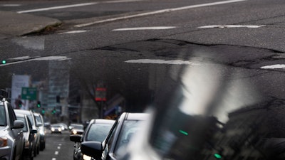 In this image taken through the reflection of a car window, a person walks along W Burnside Street near a repaired patch in the road on Thursday, Feb. 6, 2025, in Portland, Ore.