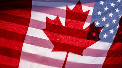 Sunlight shines through the flags of Canada and the United States, held together by a protester outside on Parliament Hill in Ottawa, Feb. 1, 2025.