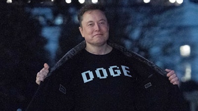 Elon Musk flashes his T-shirt that reads 'DOGE' to the media as he walks on South Lawn of the White House, in Washington, March 9, 2025.