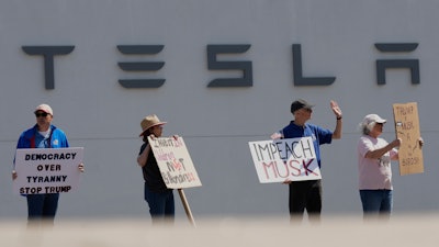 Demonstrators protest against Elon Musk and Department of Government Efficiency cuts outside a Tesla dealership, Saturday, April 12, 2025, in Kansas City, Mo.