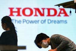 A woman wearing a protective mask to help curb the spread of the coronavirus works near the logo of Honda Motor Company at a showroom on May 13, 2021, in Tokyo.