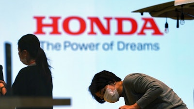 A woman wearing a protective mask to help curb the spread of the coronavirus works near the logo of Honda Motor Company at a showroom on May 13, 2021, in Tokyo.