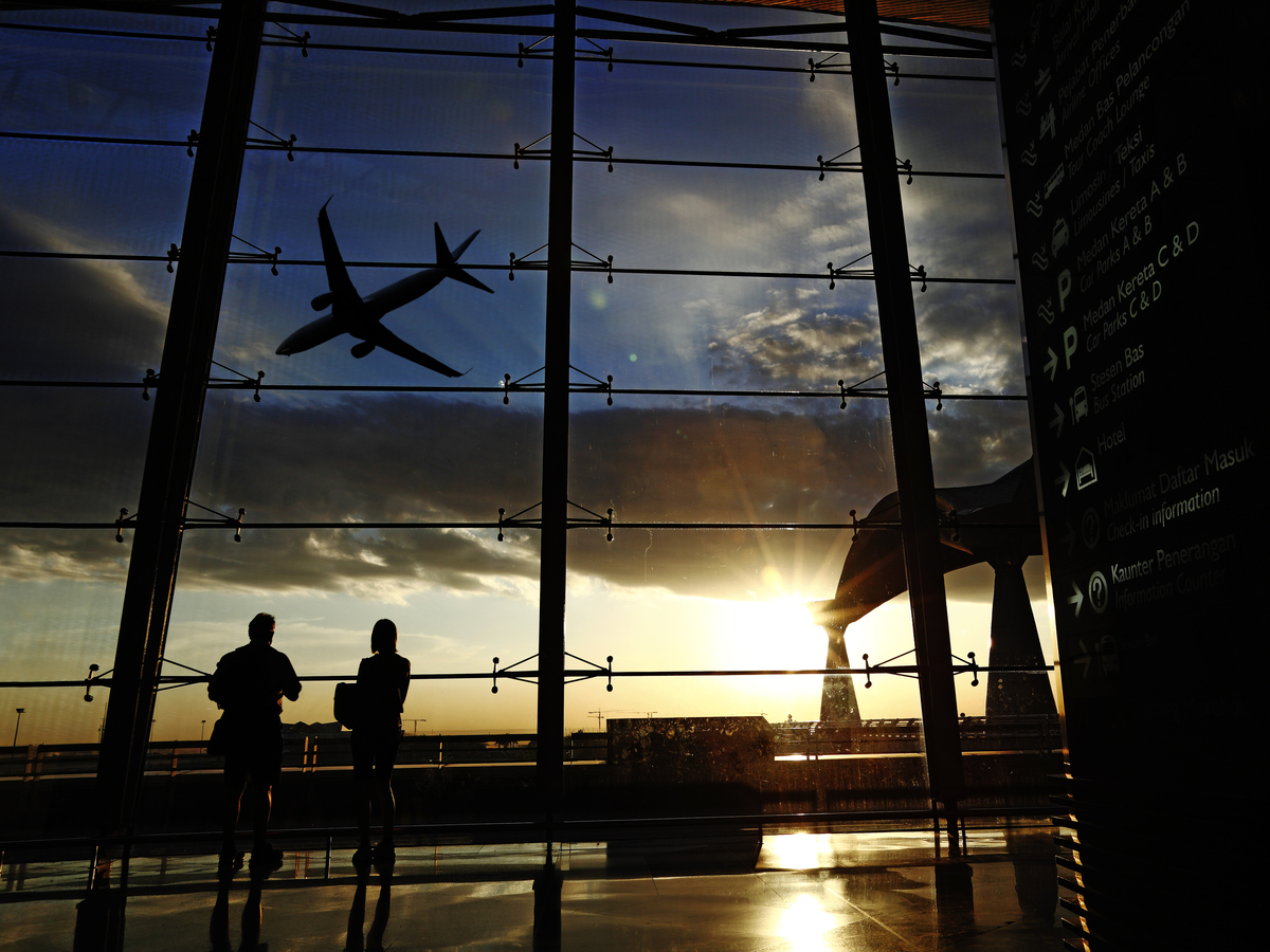 Passengers in an airport lounge watch a plane fly off at dusk. Photo: Shutterstock.