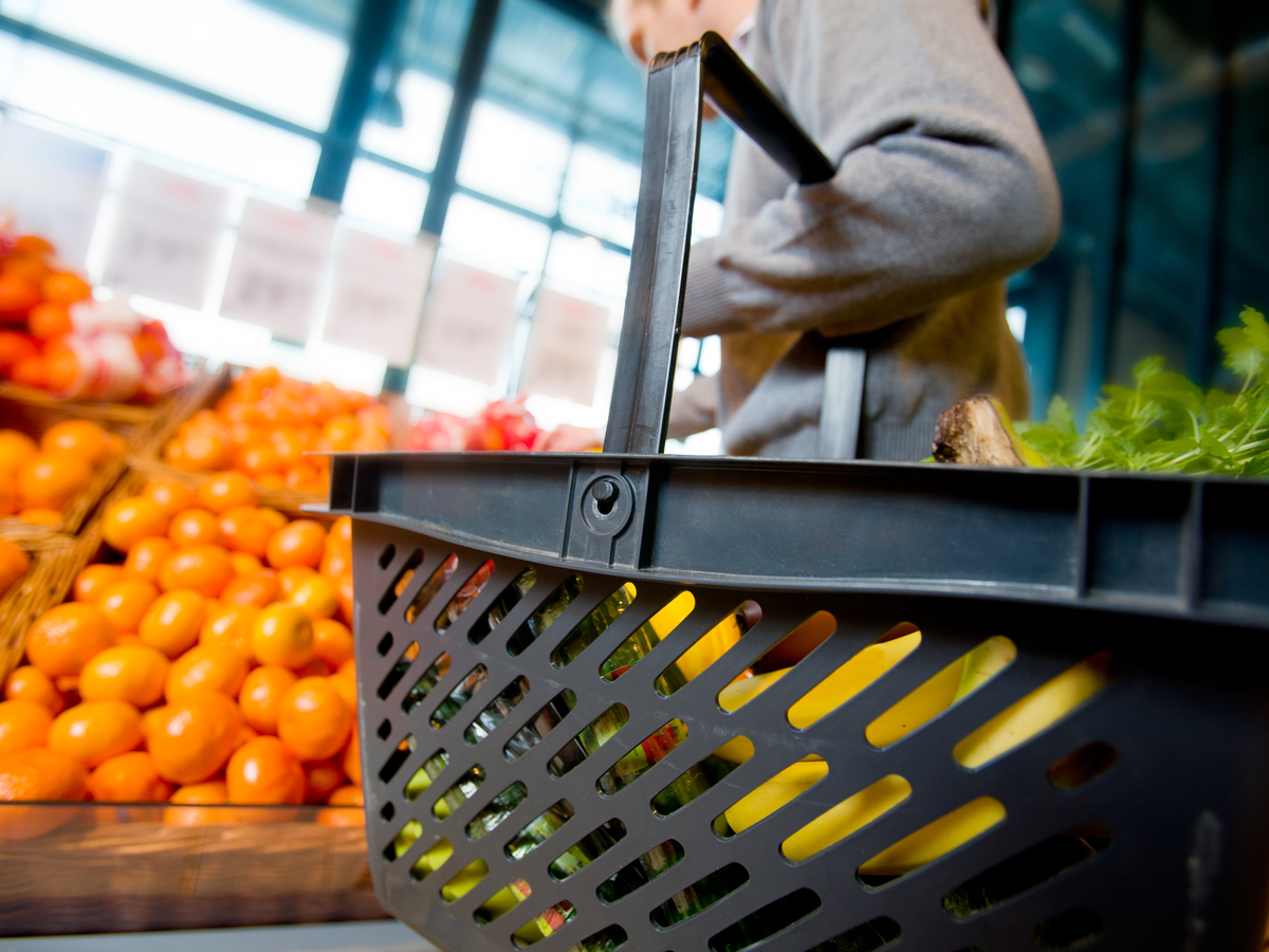 A shopper carries a basket in a grocery store. Photo: Shutterstock.