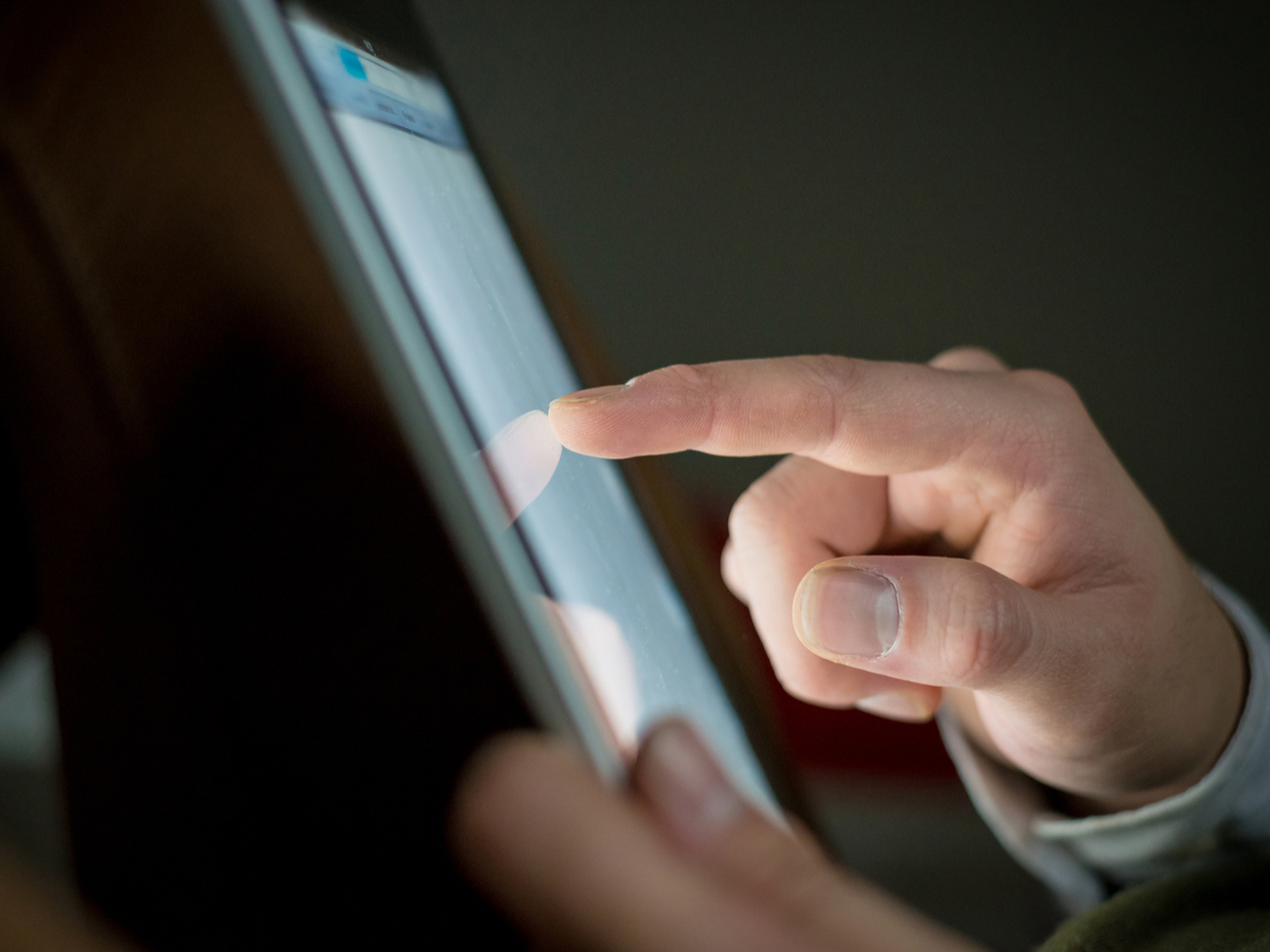 A close-up view of a person touching a digital tablet. Photo: Shutterstock.