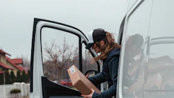 A delivery driver holding a package exits her van. Photo: Pexels.