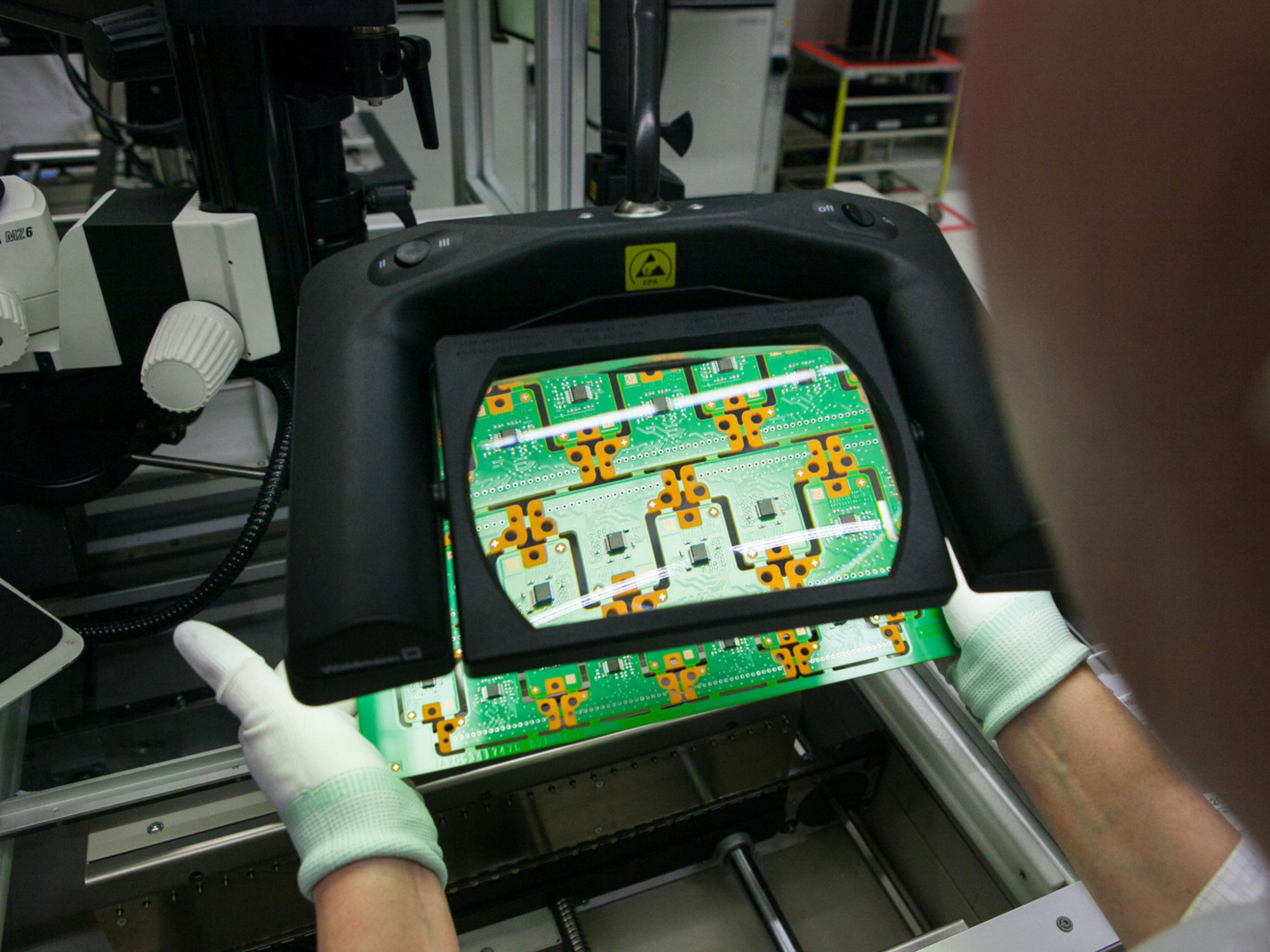 An employee holds a circuit board inside a Continental AG automotive factory. Photo: Bloomberg.