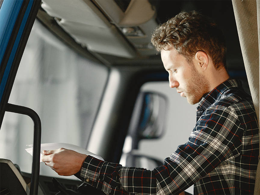 A young truck driver reads through documents. Photo: Oleg Baliuk/ Canva.