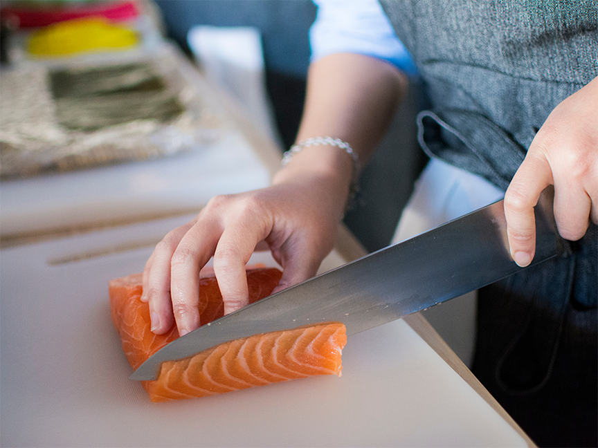 A person slices uncooked salmon on a cutting board. Photo: Huy Phan/ Pexels.