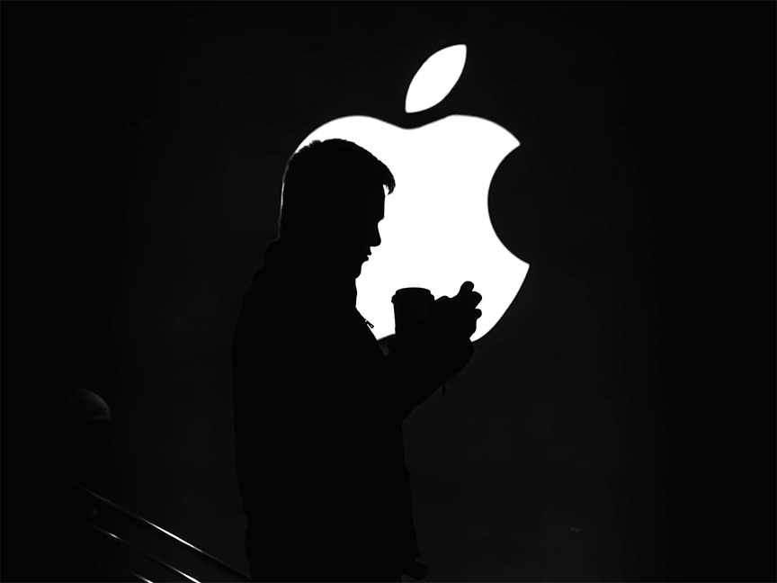 A silhouette of a person standing in front of the Apple Inc. logo. Photo: Duophenom/ Pexels.