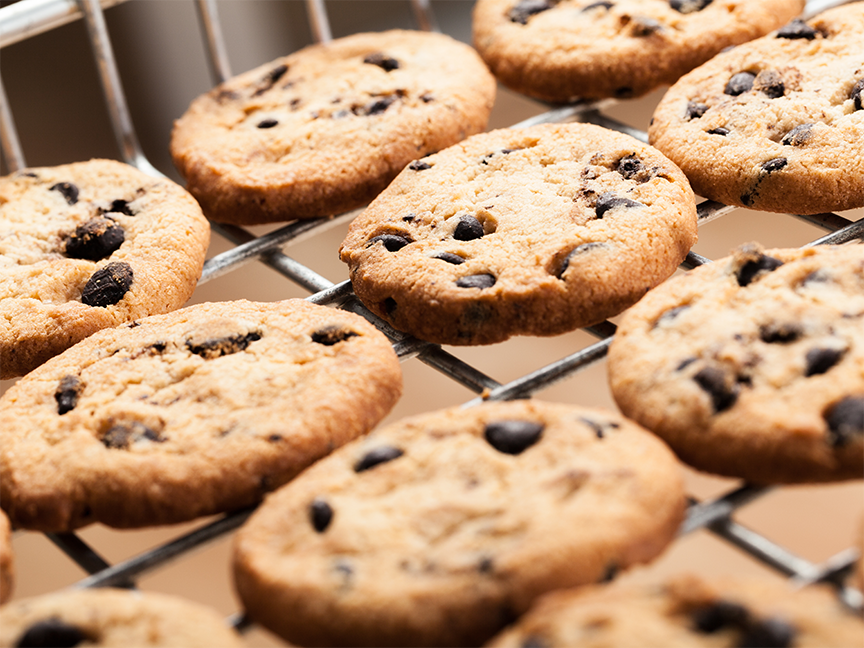 Chocolate chip cookies cool on a baking sheet. Photo: Lee Torrens/ Canva.