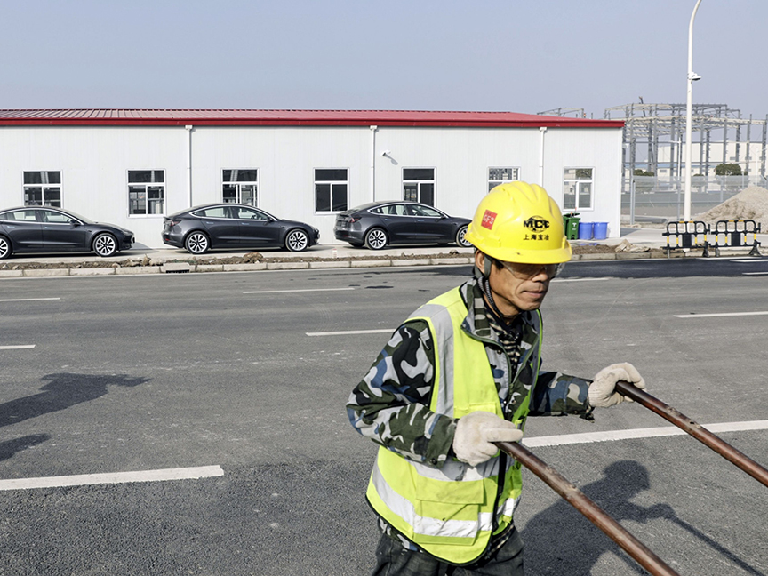 A construction worker pushes a cart past Tesla Inc. Model 3 vehicles at the company's Gigafactory in Shanghai, China. Photo: Bloomberg.