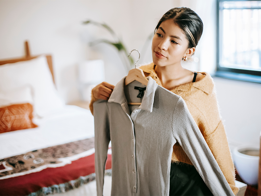A woman tries on clothes in her bedroom. Photo: Liza Summer/ Pexels.