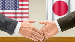 A handshake is taking place between two people with the flags of the United States and Japan in the background. Photo: iStock.com/Zerbor