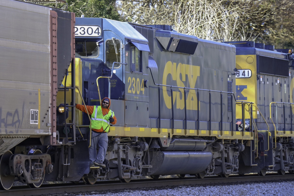 ATHENS, GEORGIA, U.S.A. - Jan 21, 2019: A railroad employee holding a walkie-talkie leans out from a CSX railroad locomotive, looking ahead up the track.