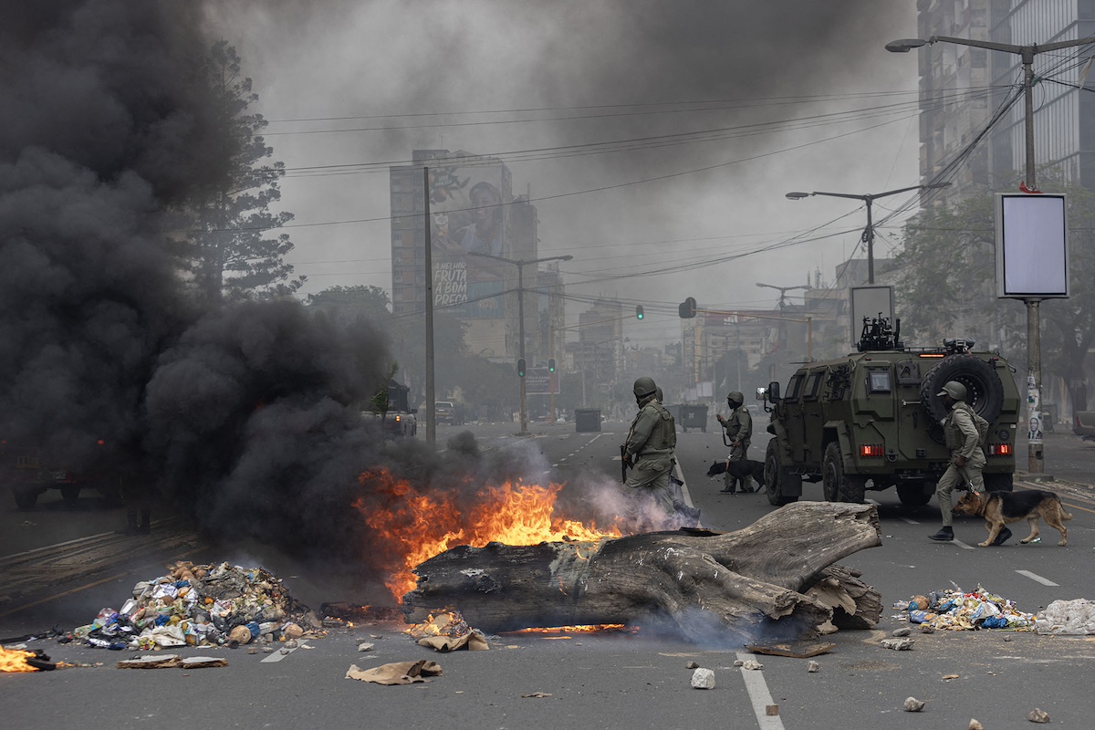 Anti-riot police officers walk past burning barricades made by protesters in Maputo, Mozambique, on November 7. Photo: Alfredo Zuniga/AFP/Getty Images via Bloomberg.
