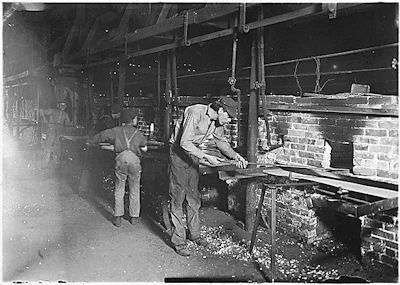 BLACK AND WHITE PHOTO OF CHILDREN IN DUNGAREES AND CAPS USING WOODEN PANELS TO LOAD AN OVEN