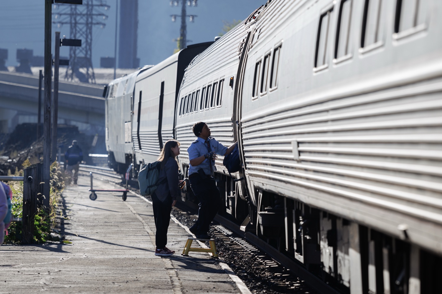 Passengers boarding an Amtrak train at a station platform with city skyline in background