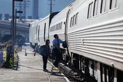 Passengers boarding an Amtrak train at a station platform with city skyline in background