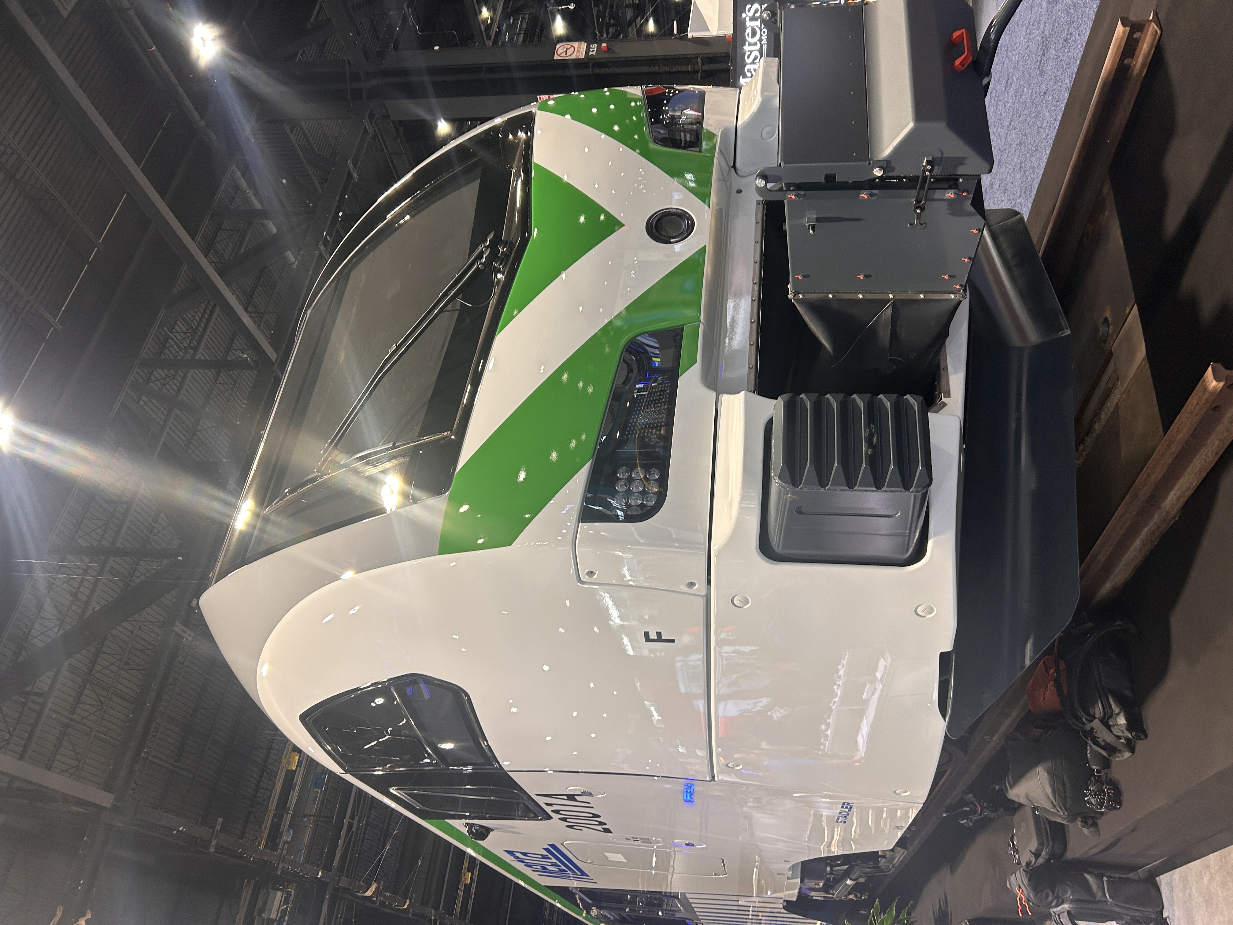 White and green recreational RV trailer displayed indoors at a trade show or exhibition venue