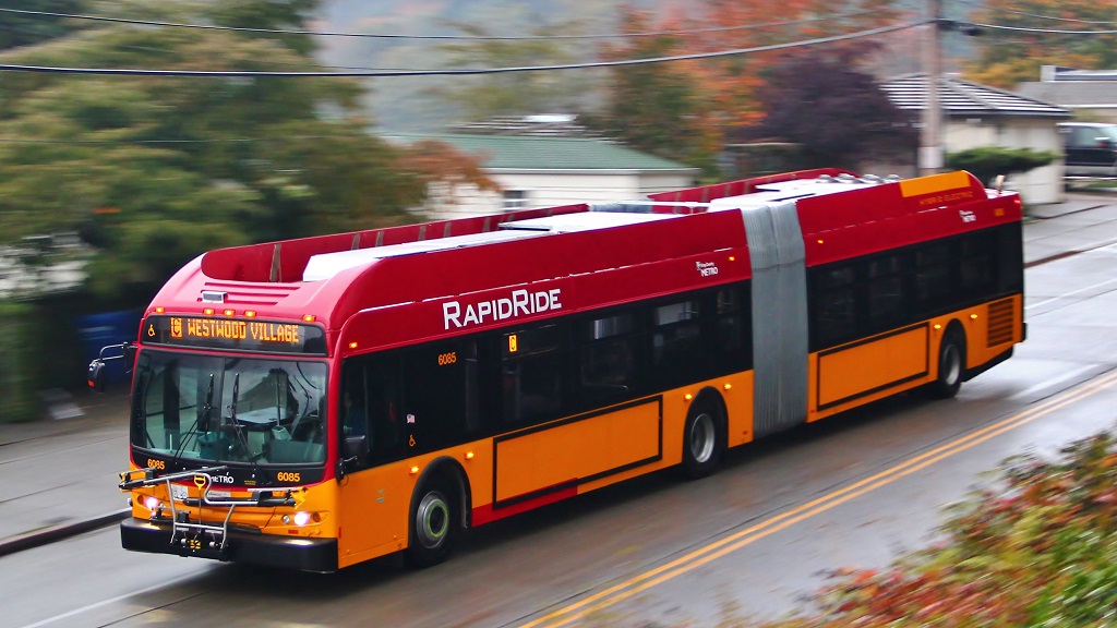 Red and orange RapidRide transit bus moving on a tree-lined street