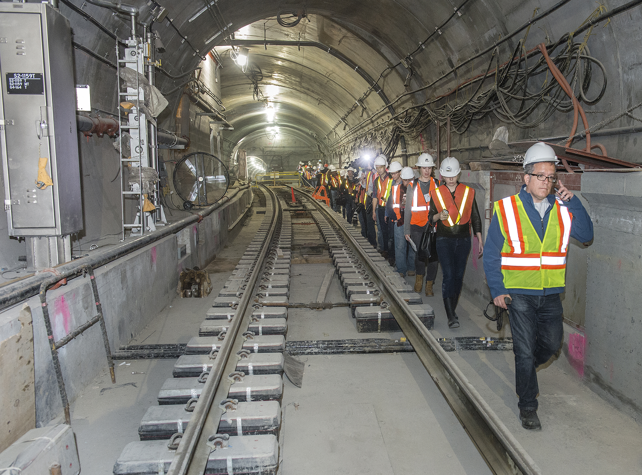 Workers in safety vests and hard hats walking through an underground transit tunnel during inspection or construction work.