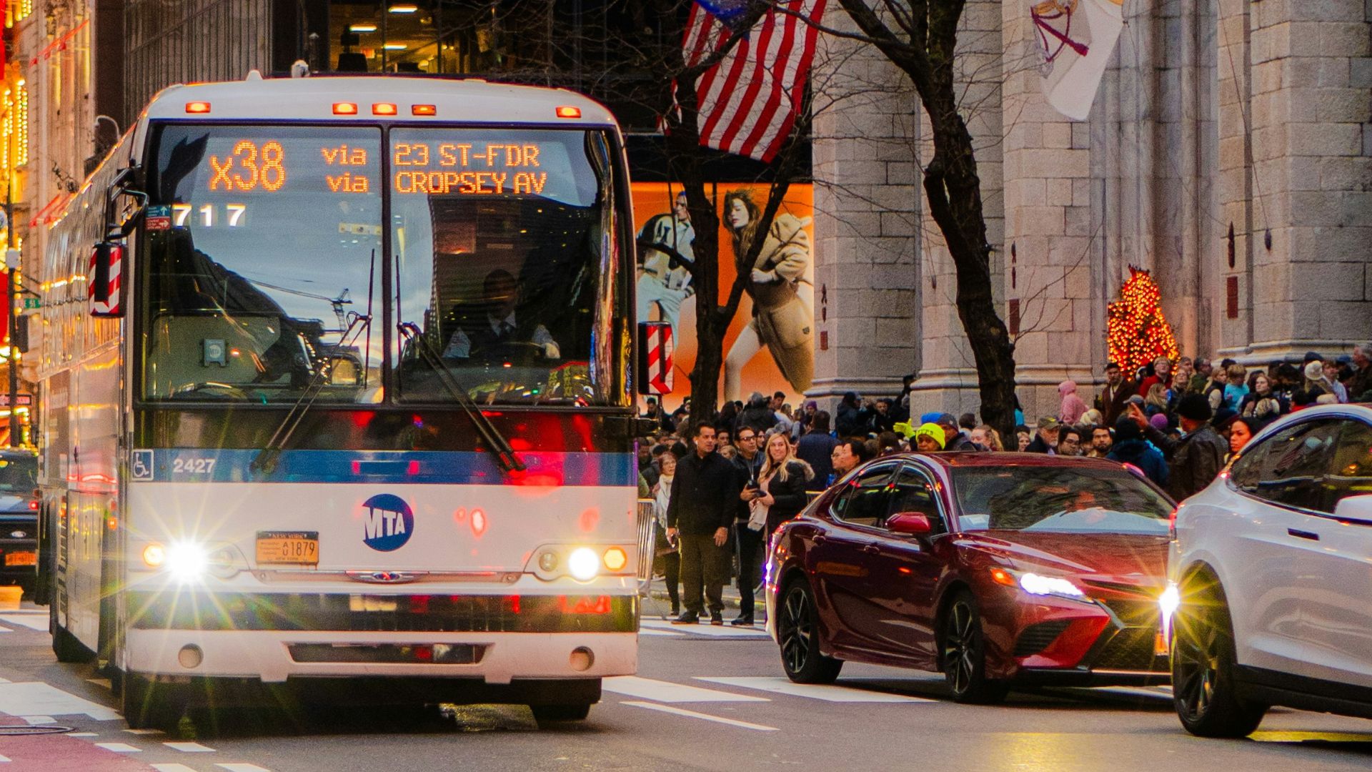 MTA bus navigating busy urban street with pedestrians and vehicles in front of decorated holiday storefront