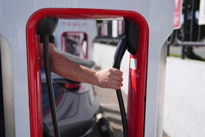 A person reaches to plug in an electric vehicle at a charging station May 22, 2025, in the City of Commerce, Calif.