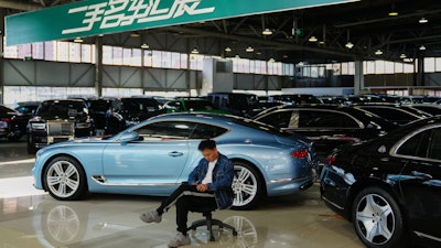 A man sits near luxury cars on offer at a second hand market in Beijing, Tuesday, Nov. 25, 2025.