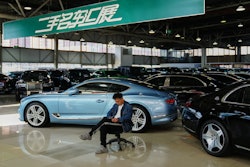 A man sits near luxury cars on offer at a second hand market in Beijing, Tuesday, Nov. 25, 2025.
