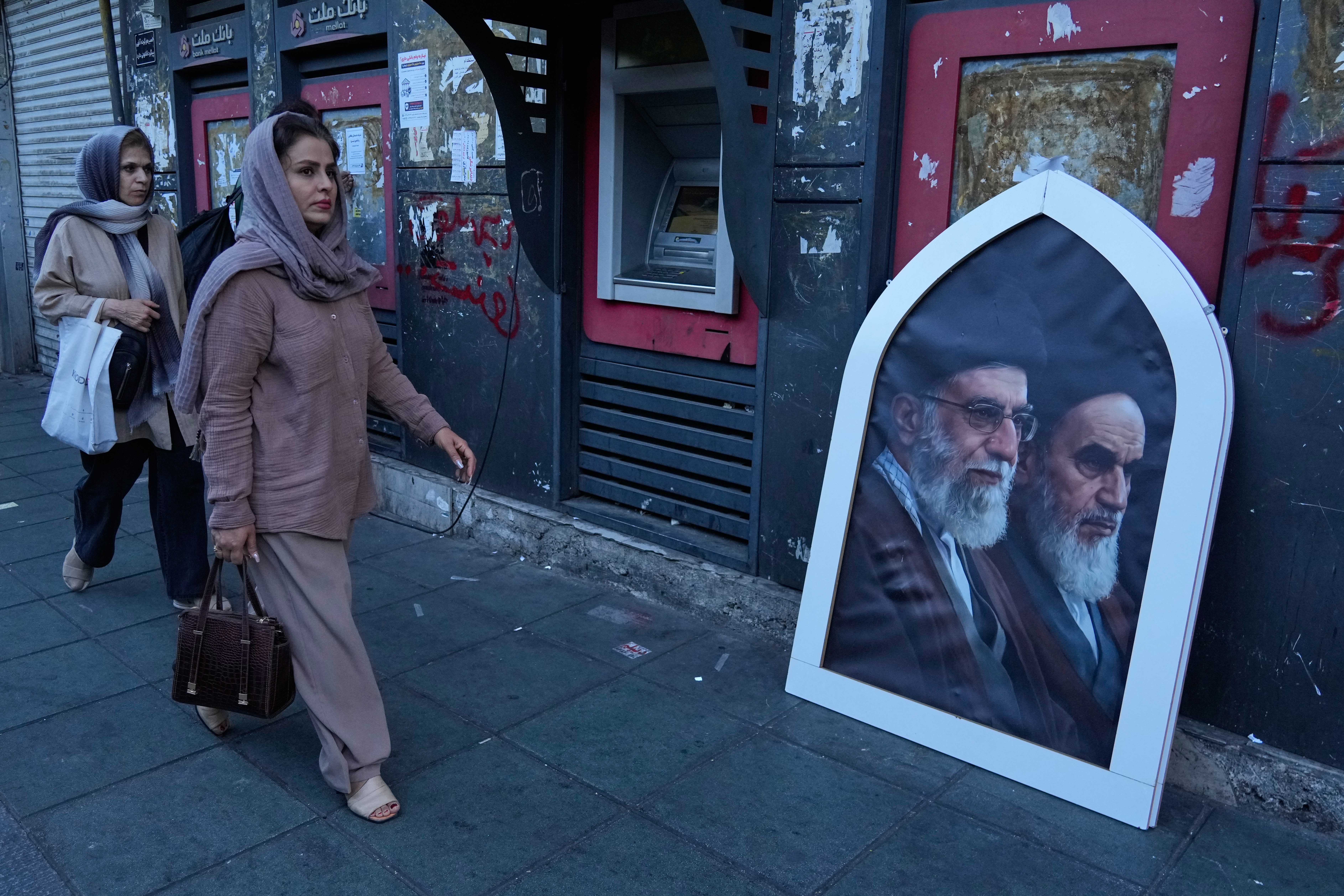 Pedestrians walk past a poster showing slain Iranian Supreme Leader Ayatollah Ali Khamenei, left, and the late revolutionary founder Ayatollah Khomeini, Islamic Revolution square, Tehran, June 14, 2026.