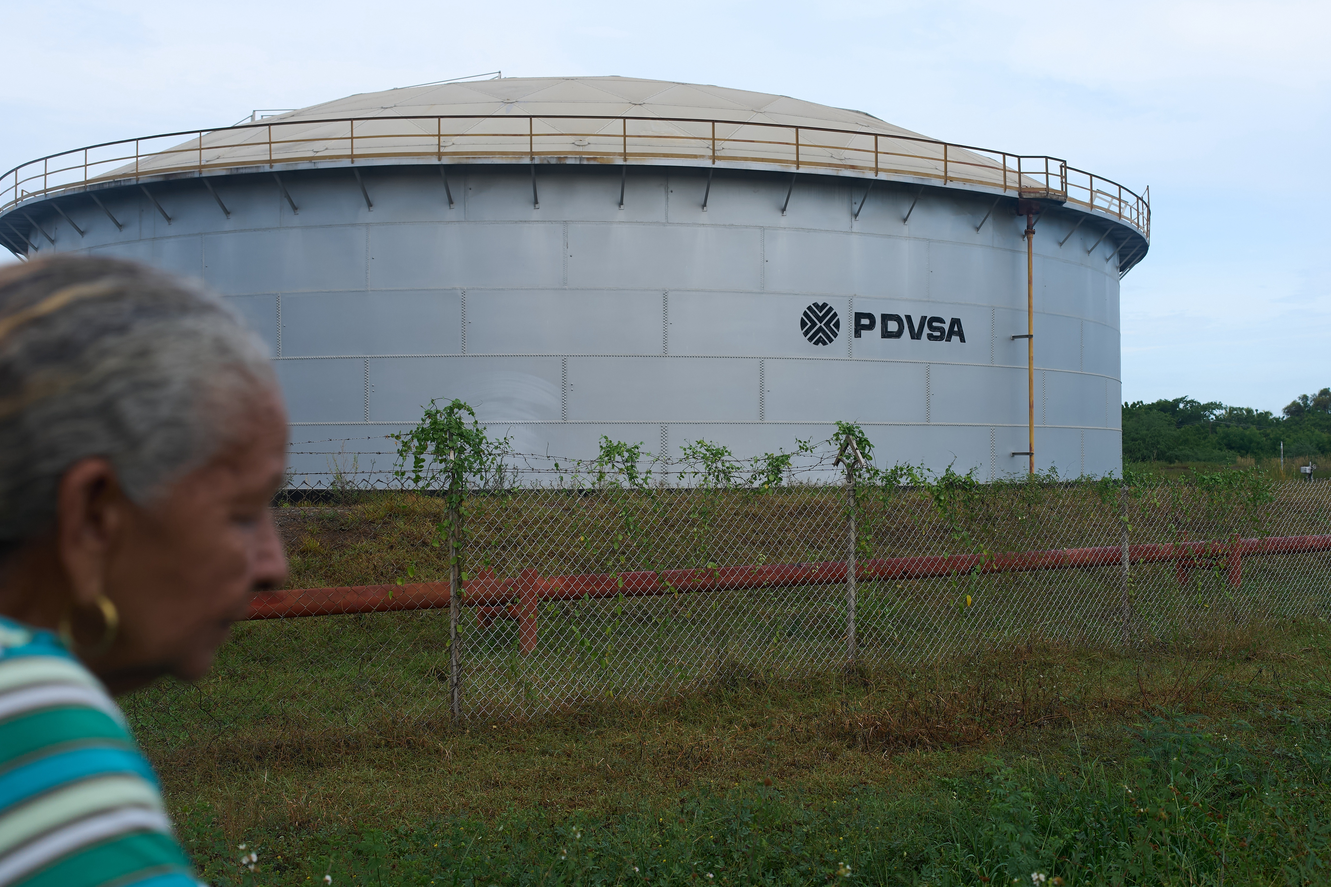 A woman walks near of a oil storage tank of Venezuela's state-run oil company, PDVSA in Cabimas, Venezuela, Tuesday, Sep. 1, 2026.